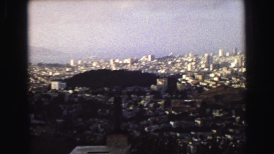 1968 Vancouver panorama from above, showing a dark wooded hill, dense neighborhoods, and distant bright city towers.