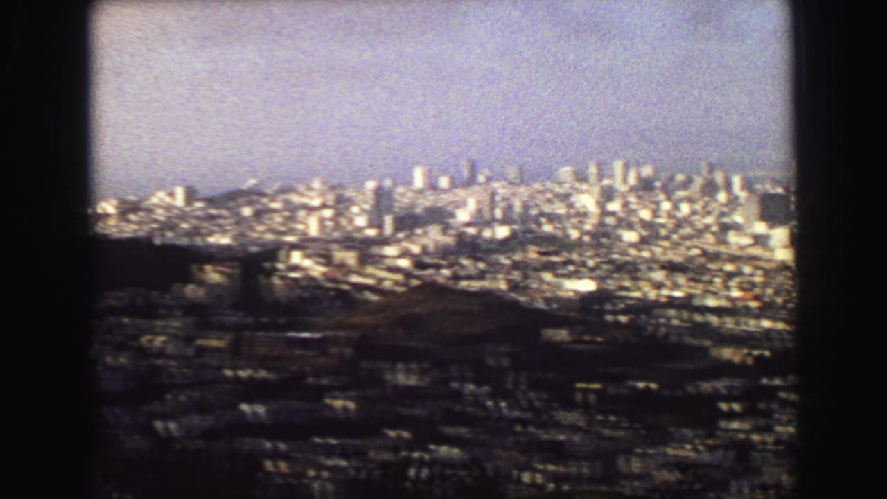 Wide 1968 8mm overlook of Vancouver, with hillside terrain in front and a dense city skyline under pale haze.