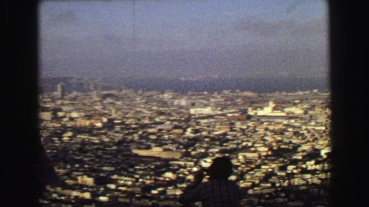 1968 Vancouver panorama with dense buildings, distant water and hills, and a silhouetted visitor looking over the city.