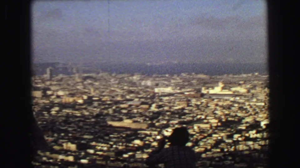 1968 Vancouver panorama with dense buildings, distant water and hills, and a silhouetted visitor looking over the city.