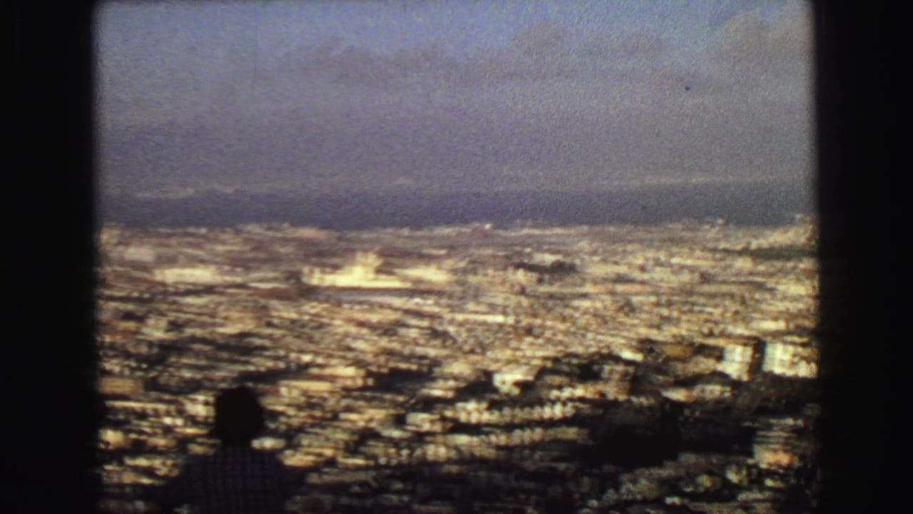 High 1968 Vancouver view over a sprawling city toward water and hills, with a small silhouetted visitor in the foreground.