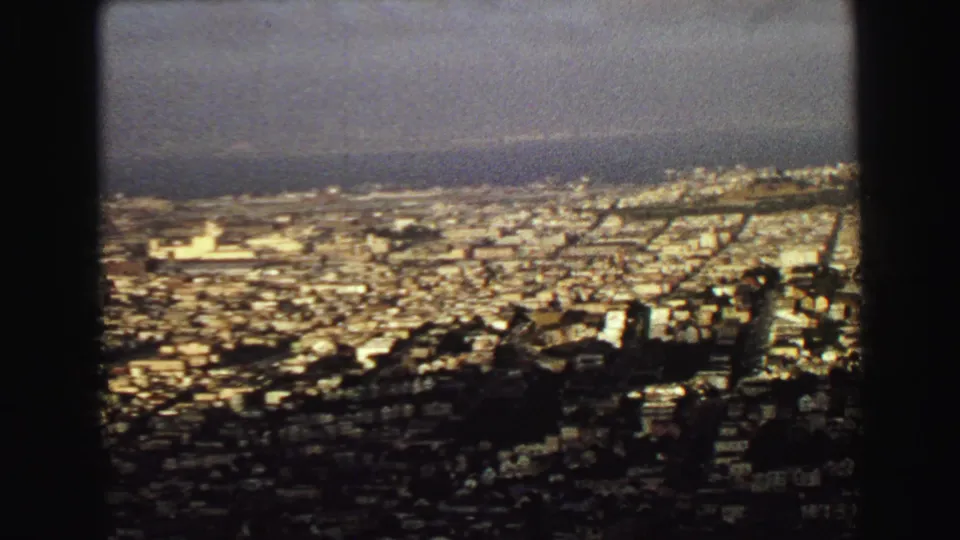 1968 8mm view over Vancouver's dense urban landscape toward water, seen through dark foreground framing.