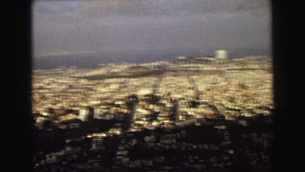 Wide cityscape with water on the horizon and a pale cylindrical structure in the distance.