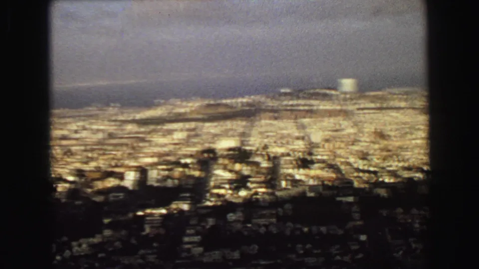 1968 Vancouver cityscape seen from above, with a distant shoreline and pale cylindrical tower or tank.