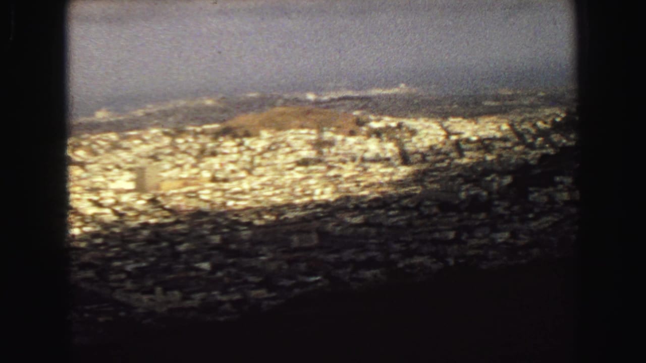 Elevated 1968 Vancouver view with bright rooftops, dark foreground edges, and a hazy coastal horizon.