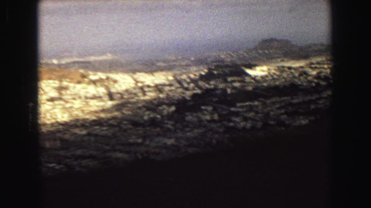 1968 Vancouver panorama frame with dark foreground, clustered buildings, and a low hazy ridge beyond the city.