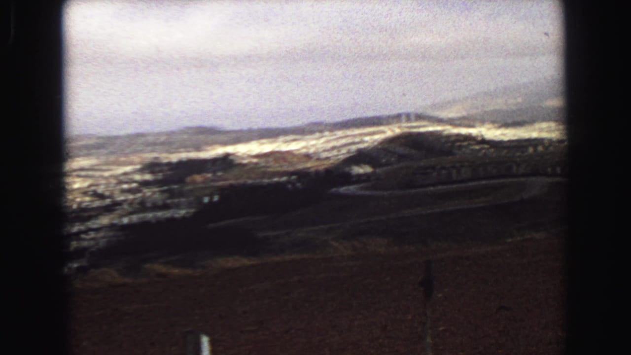 Vancouver hillside panorama on 8mm film, showing cemetery rows, open brown field, scattered buildings, distant hills, and soft haze.