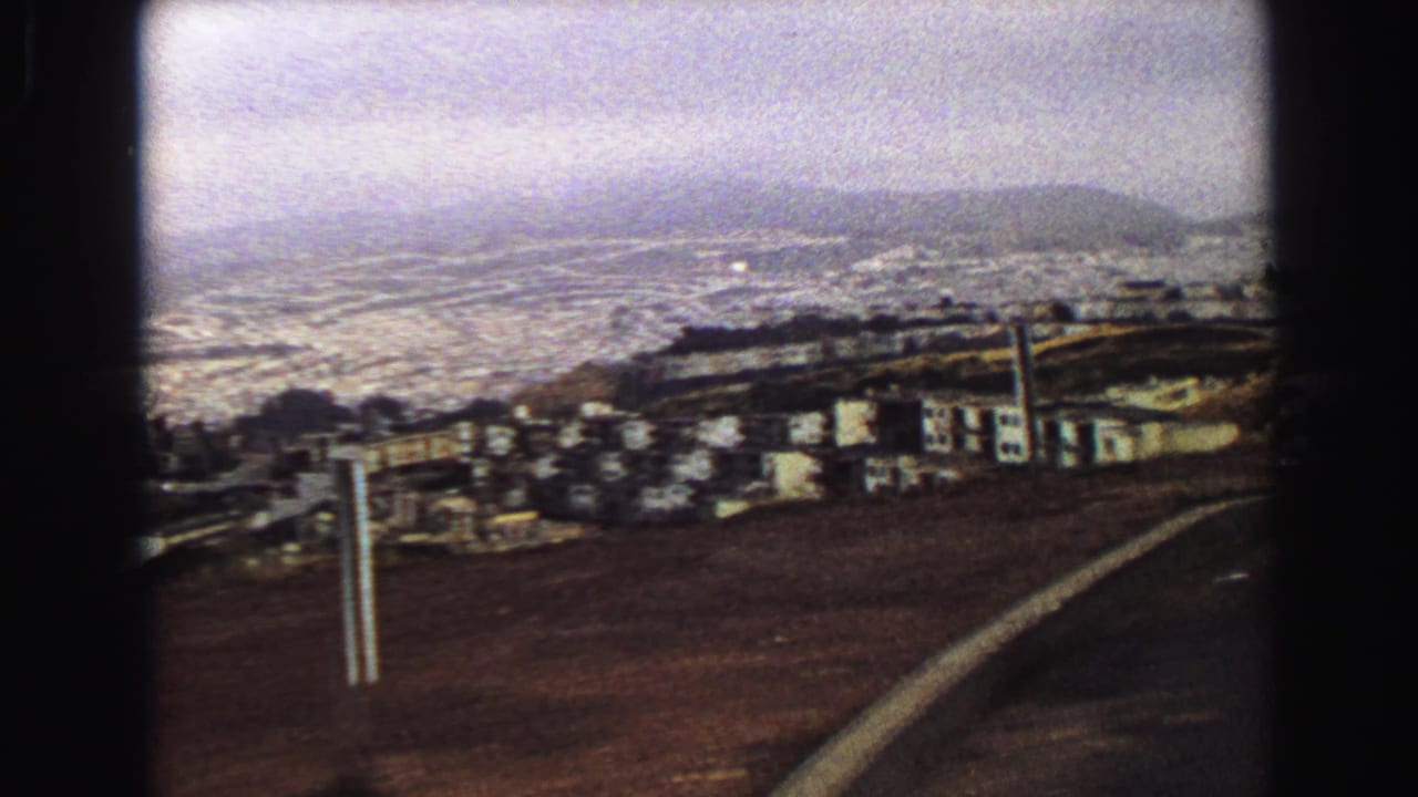 A 1968 Vancouver overlook with hillside houses, distant shoreline, low hills, and the road edge in the foreground.