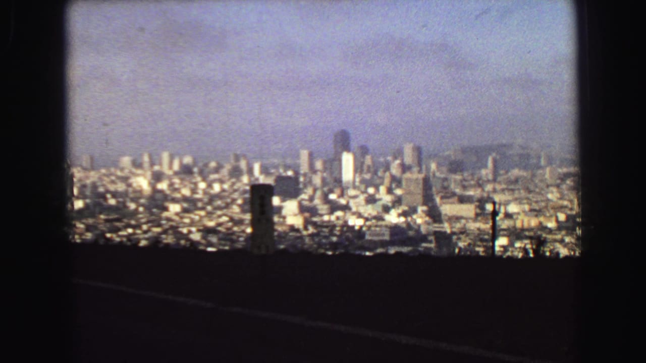 A wide 1968 8mm view looks over Vancouver's skyline and dense housing from an elevated overlook, with roadside posts in the foreground.