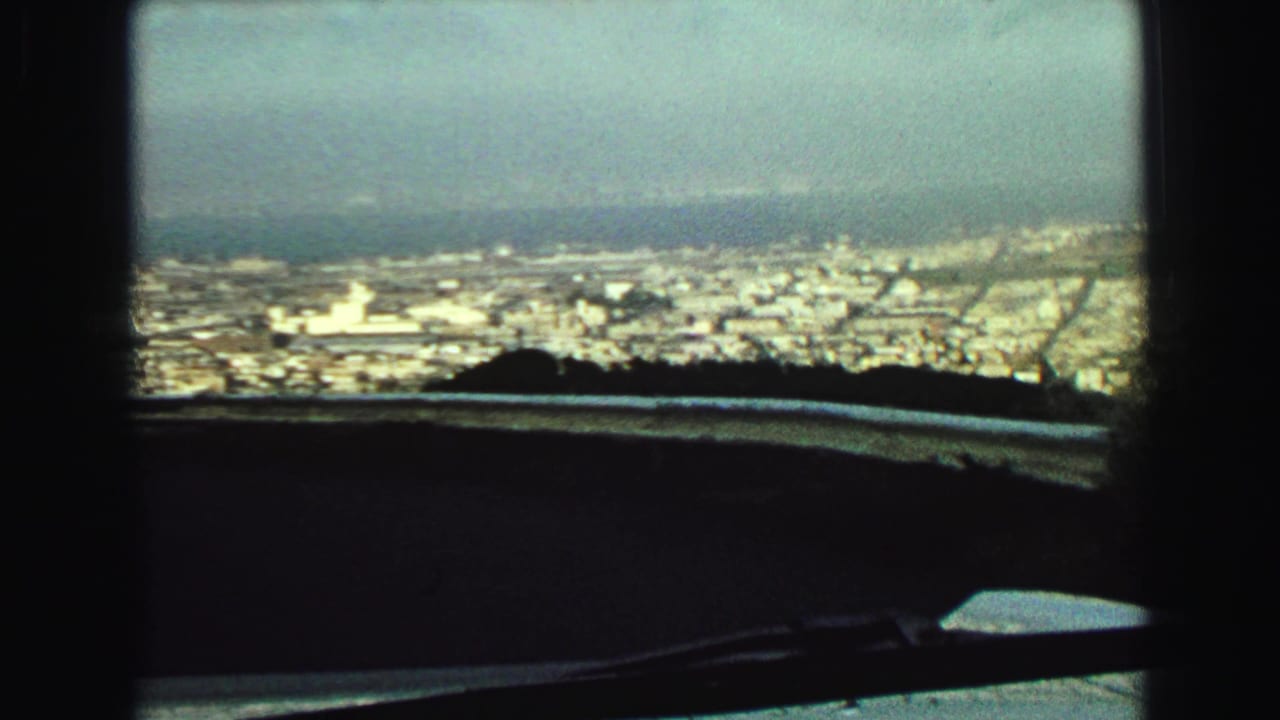 Elevated city view through a vehicle windshield with a wiper and dark dashboard in the foreground.