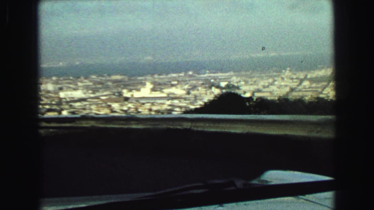 Elevated Vancouver panorama from inside a vehicle, showing dense buildings, distant water, a railing, and a wiper across the foreground.