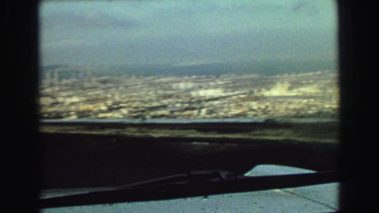 1968 Vancouver view with distant waterfront, low urban blocks, haze, dashboard edge, and windshield wiper visible at the bottom.