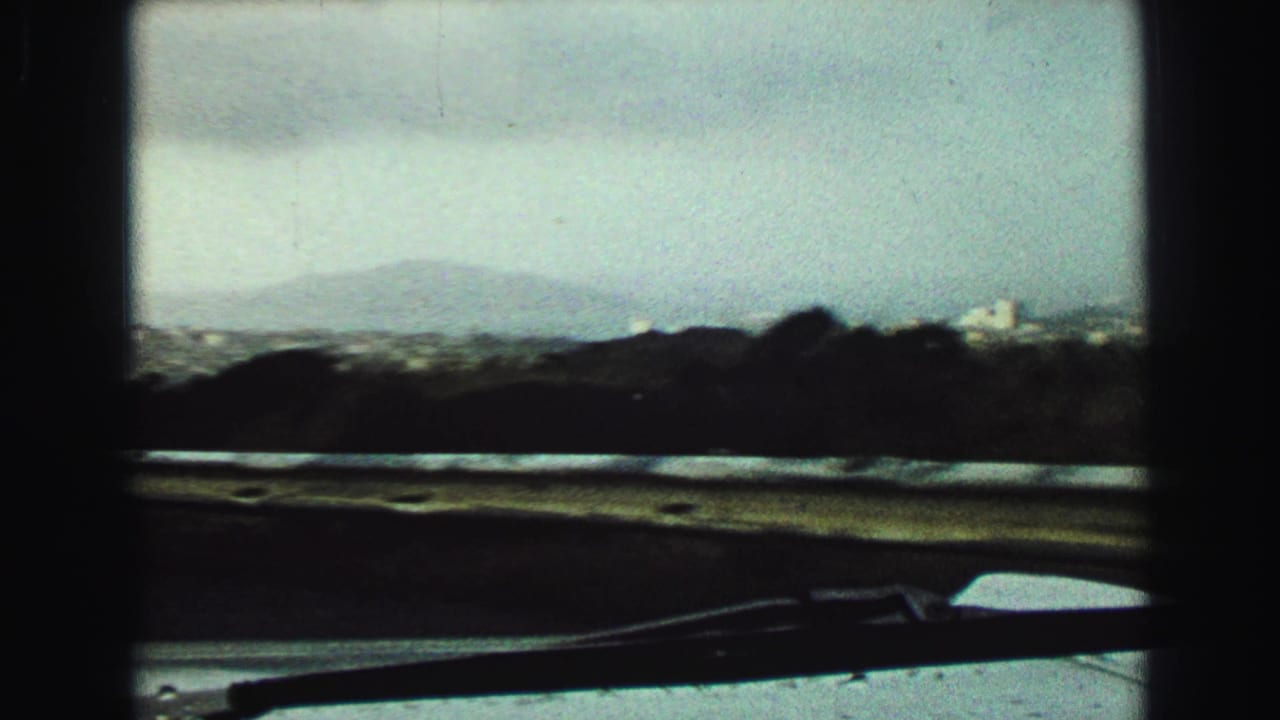 Vehicle windshield view of low hills and a hazy mountain beyond a flat foreground.