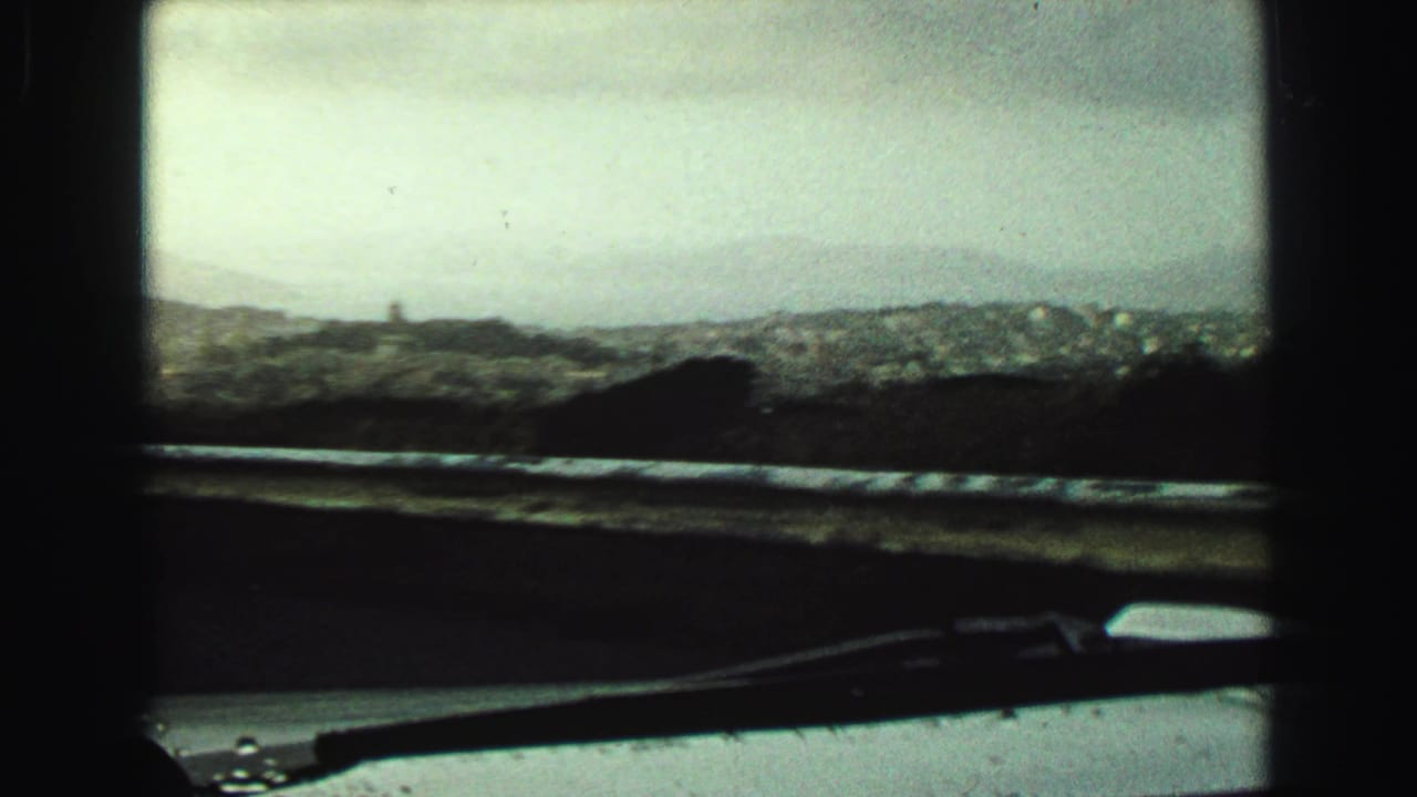 1968 Vancouver-area windshield view with hazy hills, distant buildings or shoreline, a dark dashboard edge, and a wiper in the foreground.