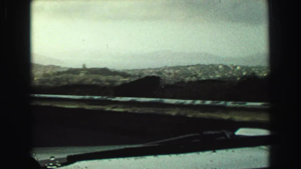 1968 Vancouver-area windshield view with hazy hills, distant buildings or shoreline, a dark dashboard edge, and a wiper in the foreground.