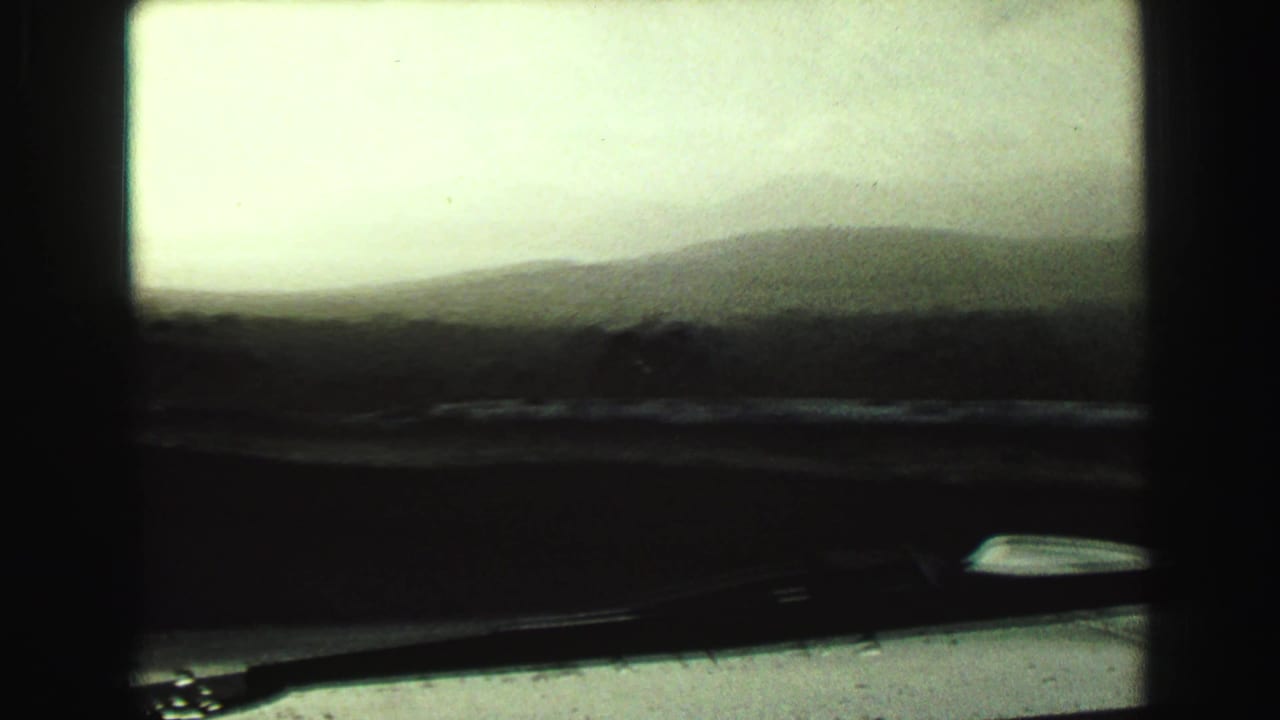 Hazy landscape seen through a car windshield with dark film borders.