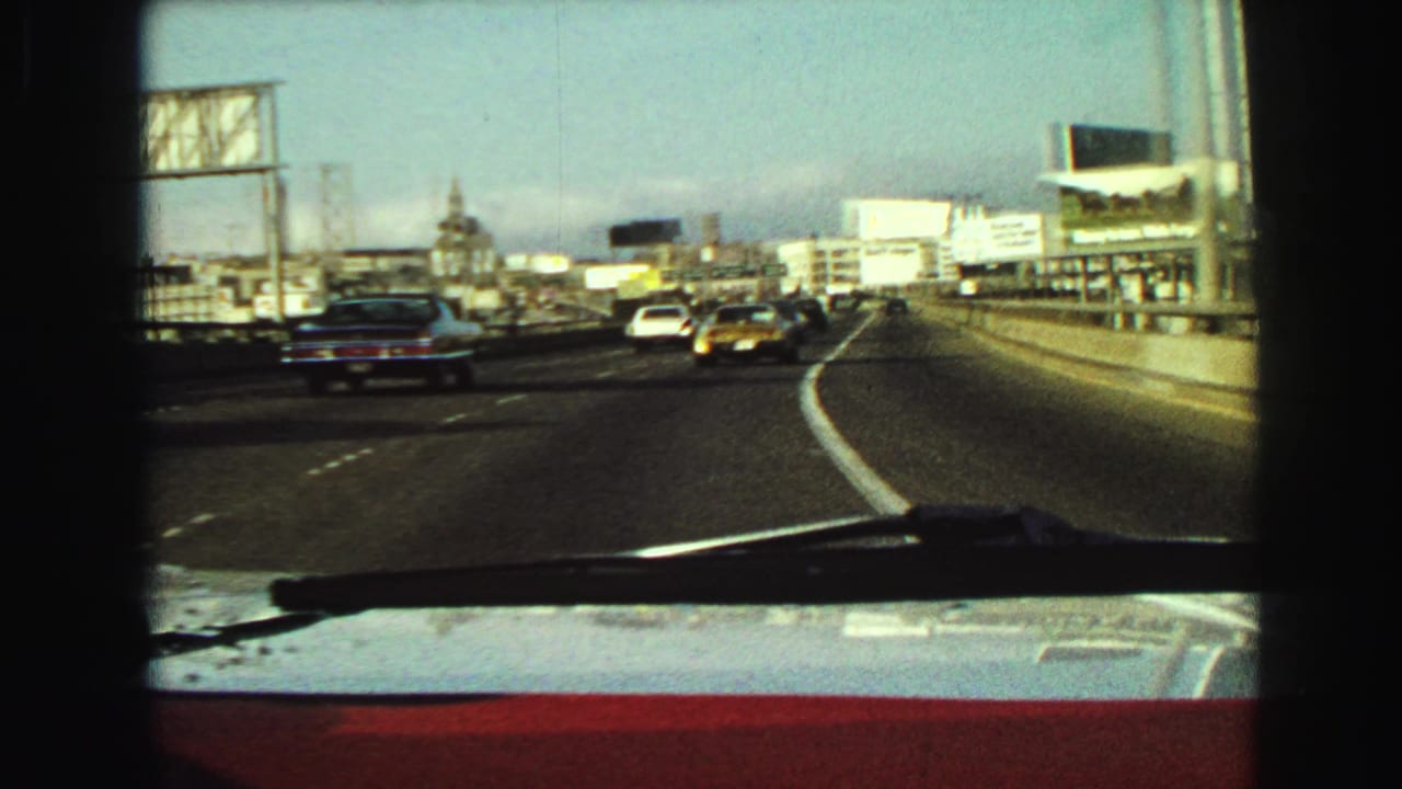 Traffic seen through a car windshield on a multi-lane urban highway with billboards ahead.