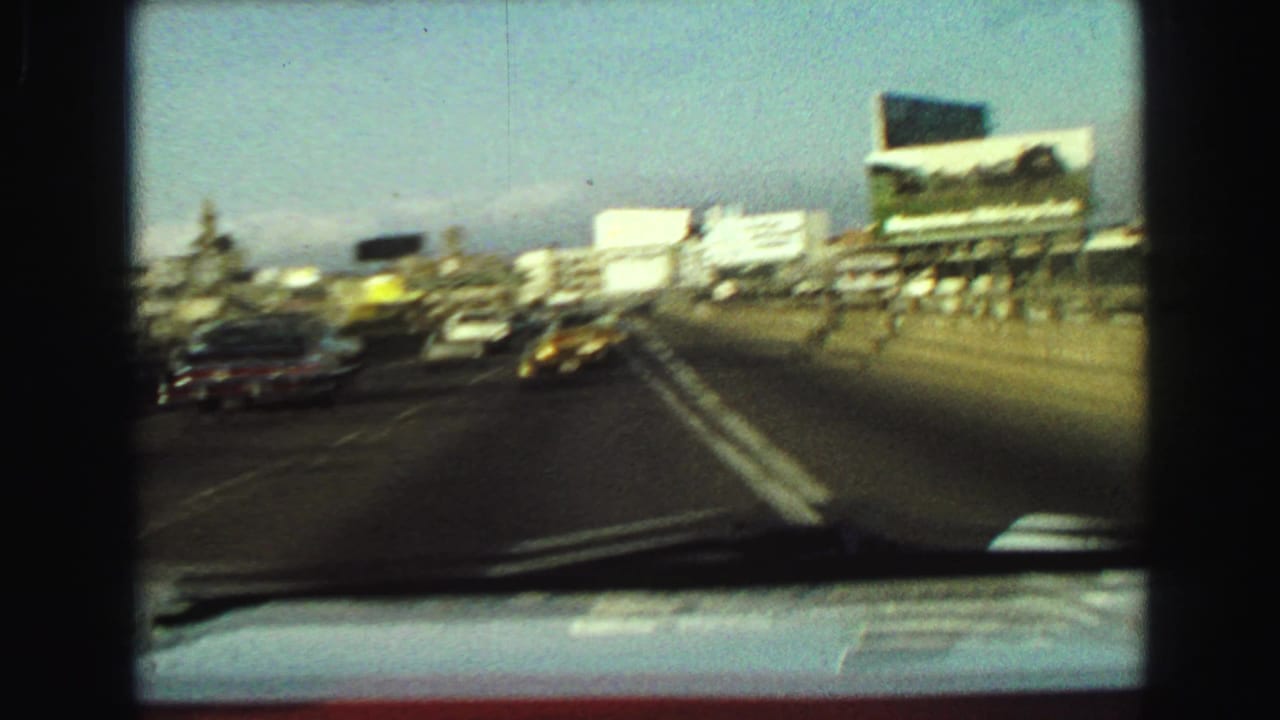 Moving 1968 Vancouver highway view with a yellow taxi, nearby cars, billboards, and windshield framing visible.