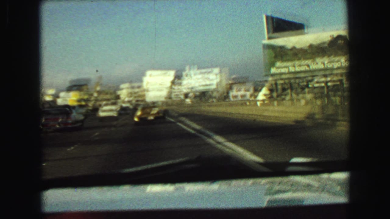 1968 Vancouver roadway scene filmed through a windshield, showing traffic, lane markings, billboards, and urban structures.