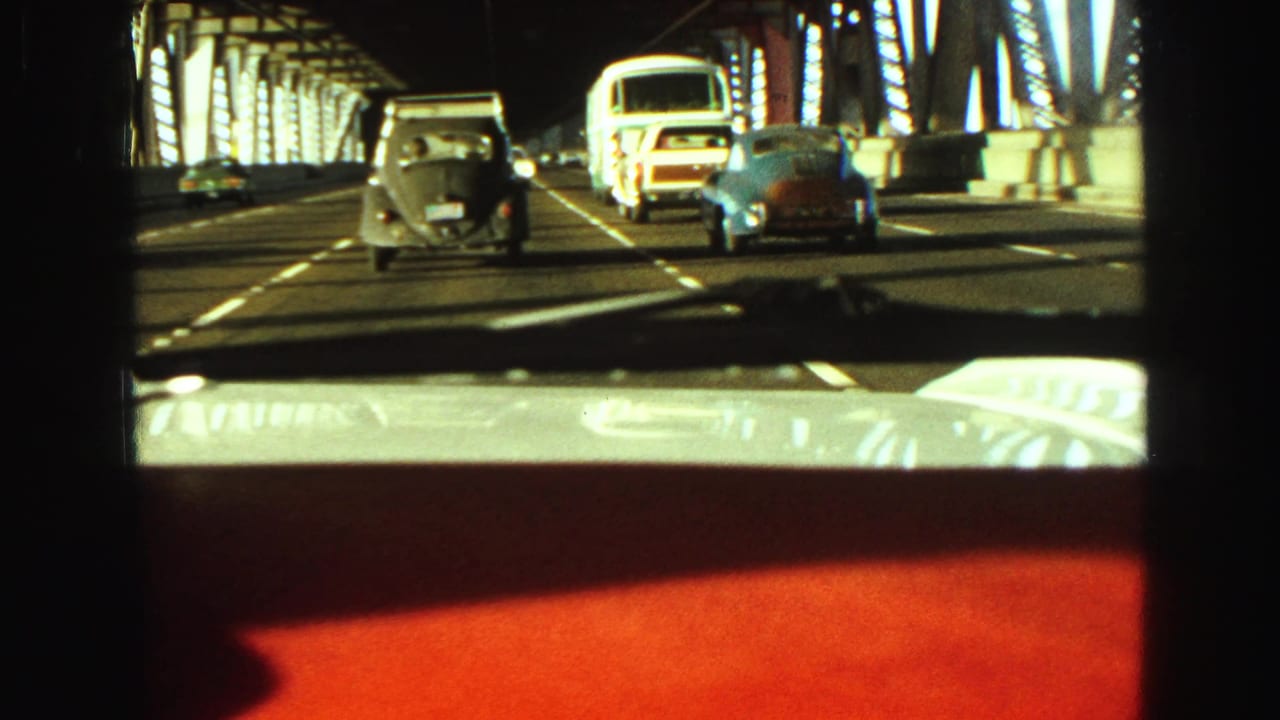 1968 Vancouver bridge crossing from inside a car, with steel trusses, a bus, and classic cars visible through the windshield.