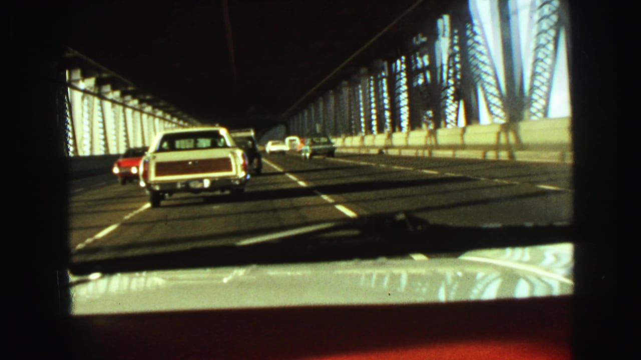 A white station wagon drives ahead on a bridge roadway.