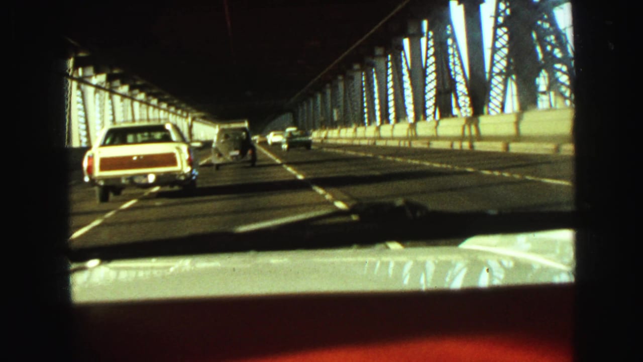 Classic vehicles continue across a Vancouver steel bridge, filmed from a moving car with dashboard and windshield visible.