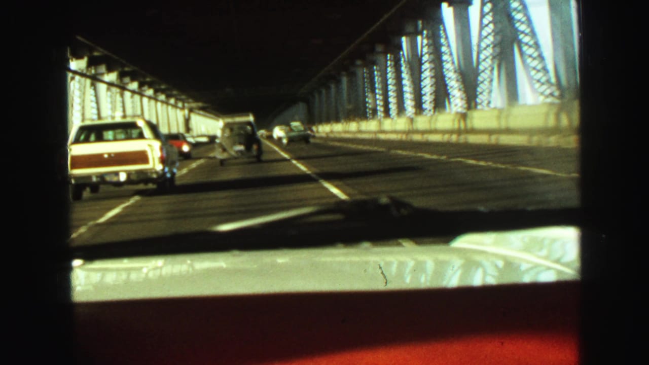 Forward-facing 1968 Vancouver driving footage shows cars on a multi-lane steel bridge with strong sunlight and shadows.