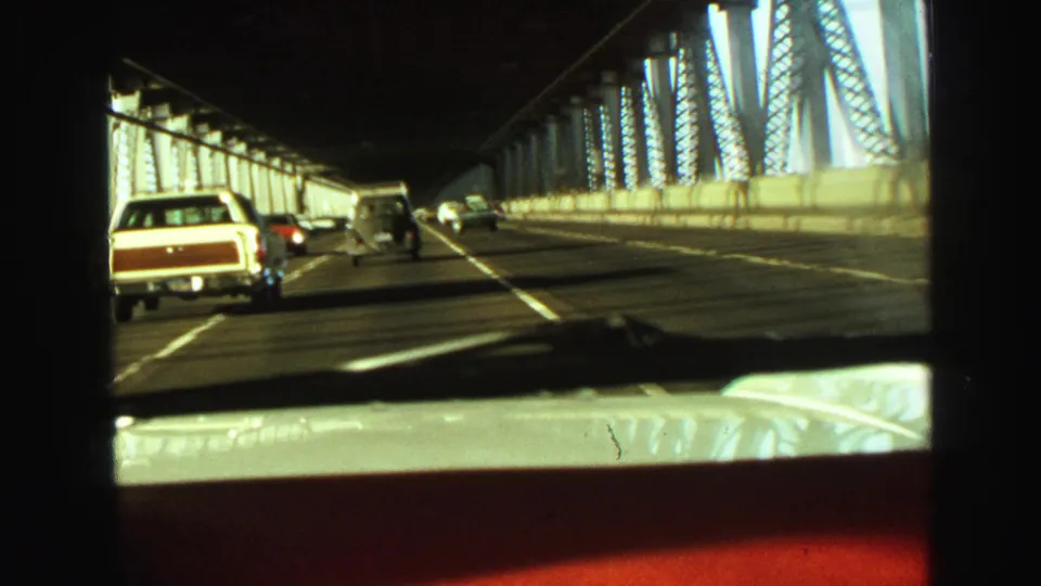 Forward-facing 1968 Vancouver driving footage shows cars on a multi-lane steel bridge with strong sunlight and shadows.
