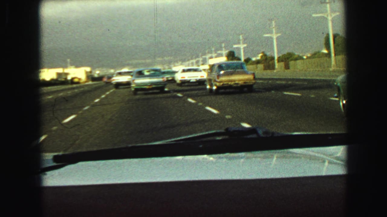 In-car 8mm view of late-1960s freeway traffic near Vancouver, with a white car, blue sedan, and gold sedan visible ahead.