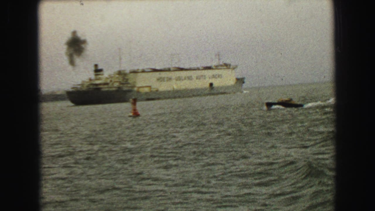 1968 Vancouver harbor scene with the tan ocean liner in the distance and a black speedboat leaving a white wake near a red buoy.