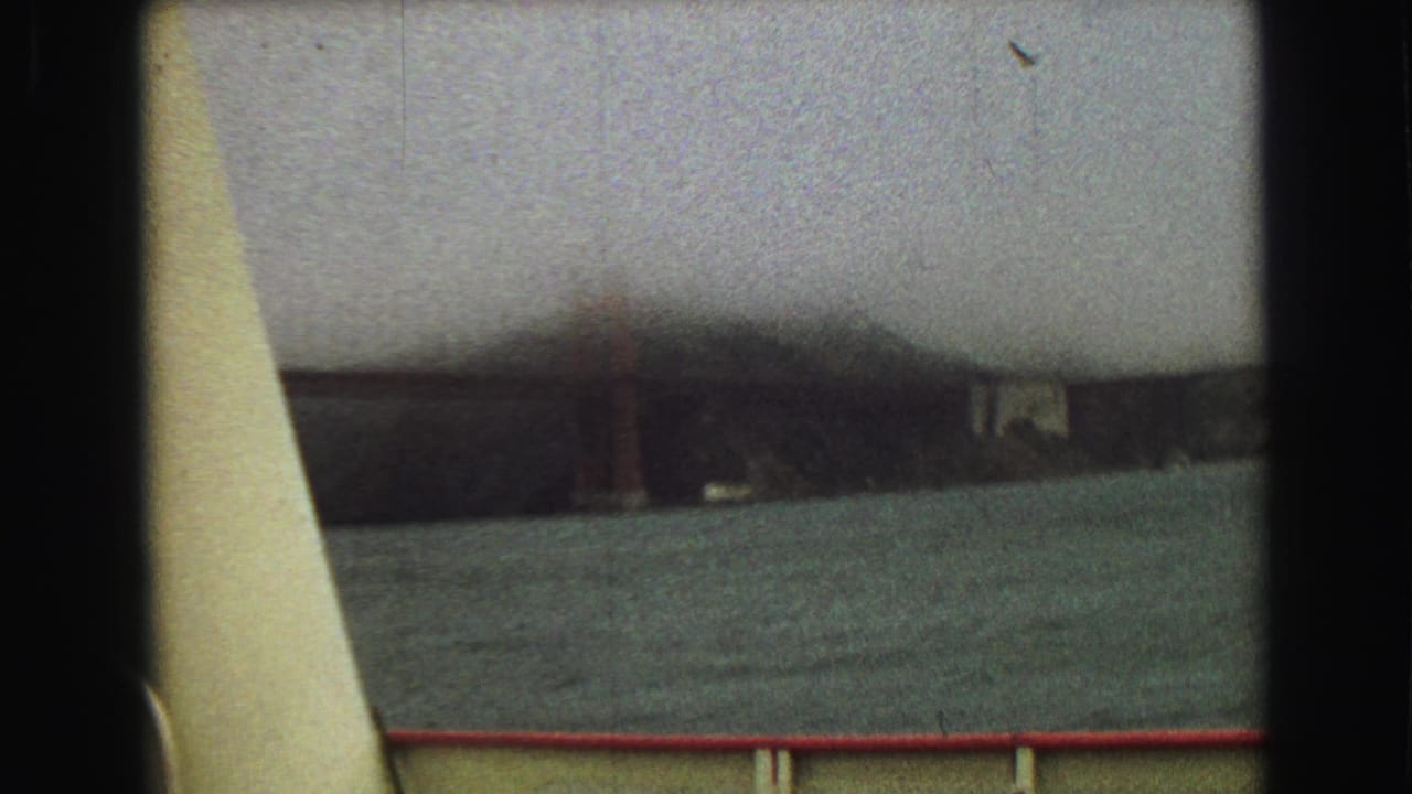 Foggy bridge span seen across water from behind a boat railing.