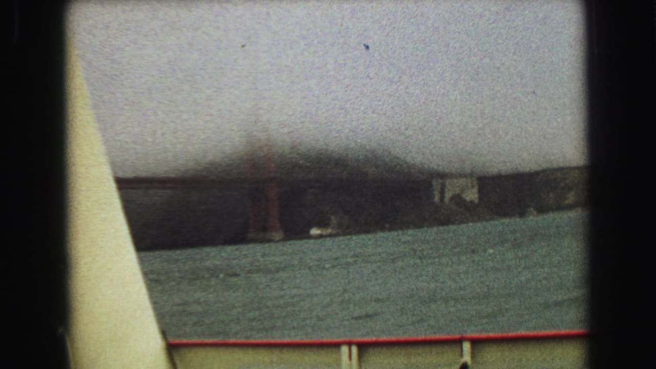 Distant bridge and fog over water with boat railing in the foreground.