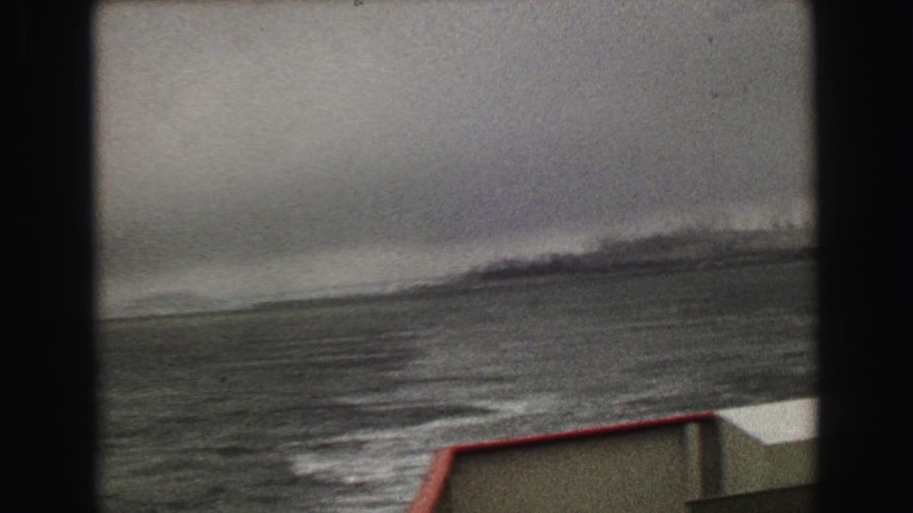 Choppy water and hazy shoreline seen past a red-trimmed boat deck.