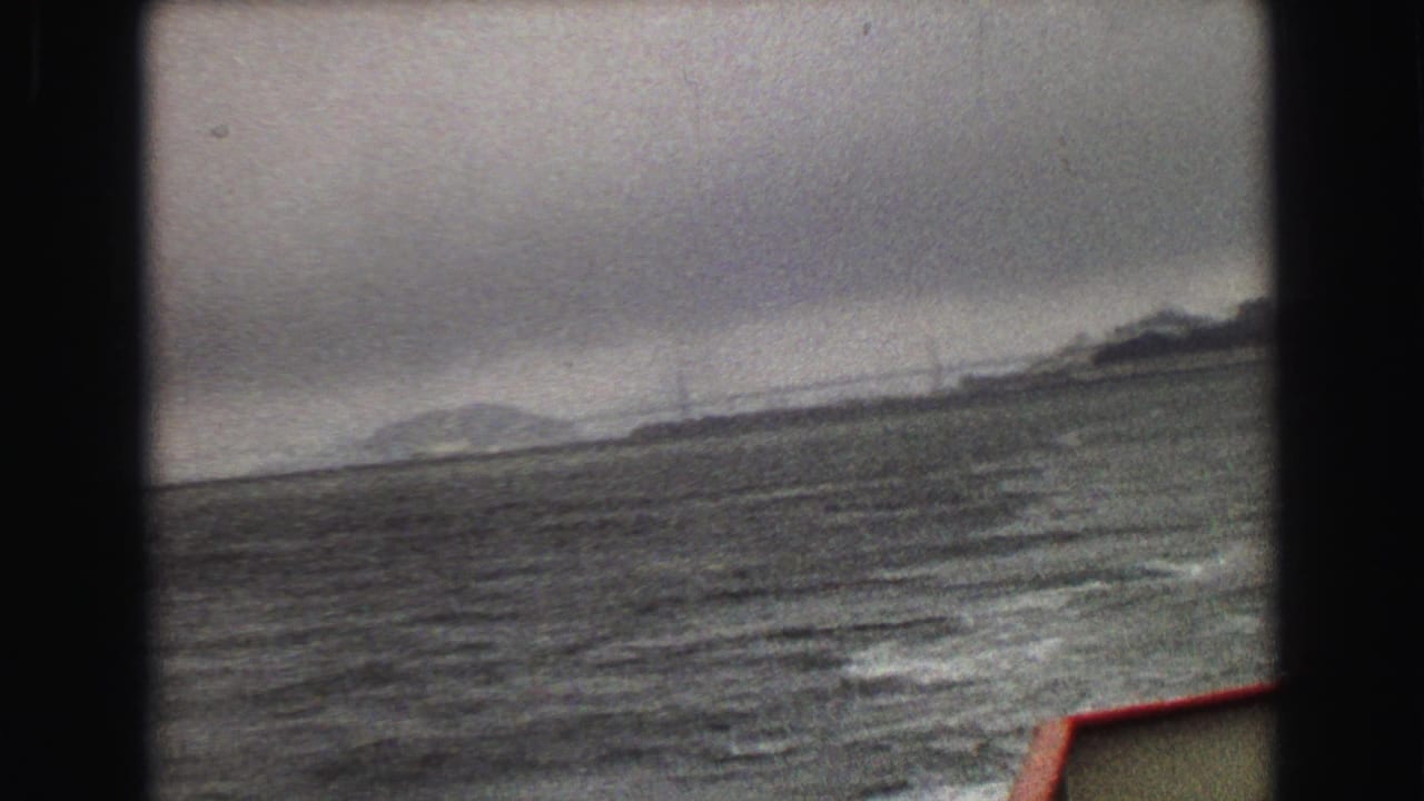 The 8mm frame appears to show a distant bridge or tower structure across Vancouver-area water under a cloudy sky.