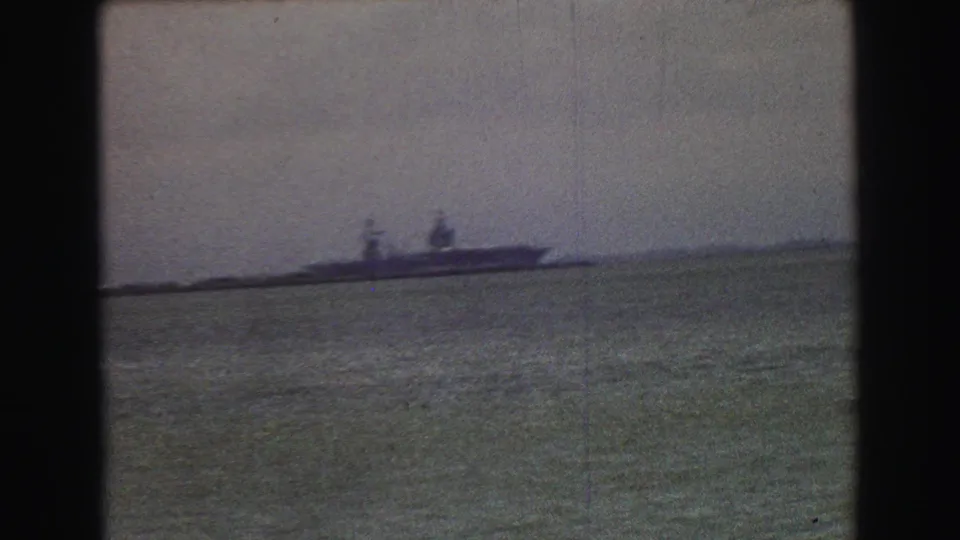 1968 8mm frame showing a distant ship on open water, filmed with heavy grain, soft focus, and muted color.