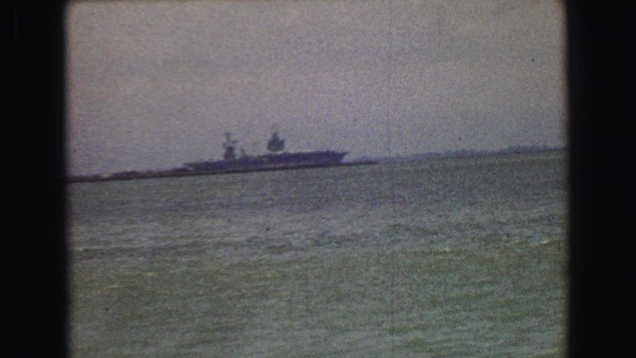 Distant ship on open water under a pale sky, seen through a dark film frame border.