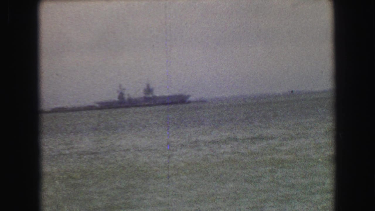 A distant ship on coastal water appears in a soft 8mm frame, with faint horizon details and dark film borders.