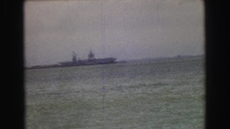 A distant ship on coastal water appears in a soft 8mm frame, with faint horizon details and dark film borders.