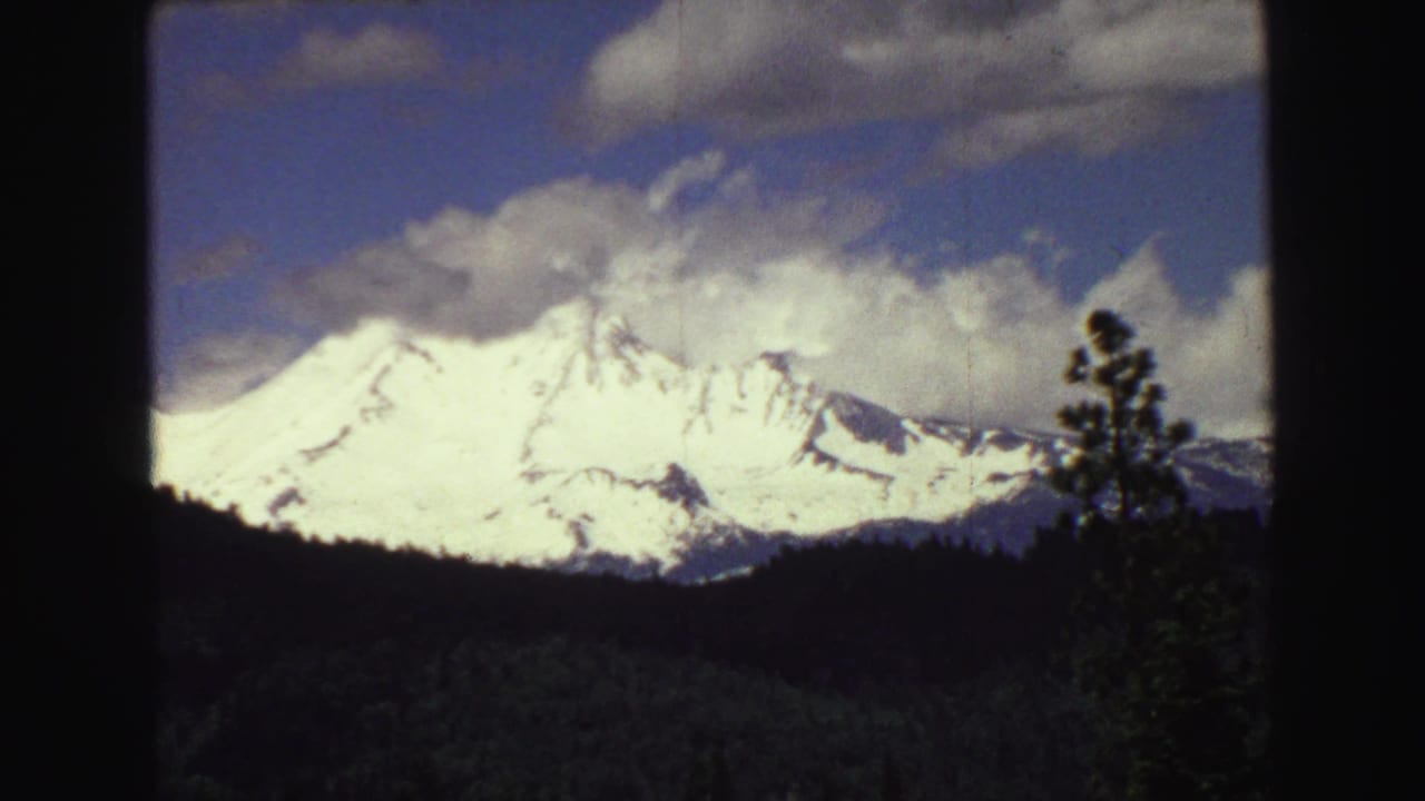 1968 8mm close landscape view near Vancouver, showing a bright snow-covered mountain above a dark forested slope and clouded sky.