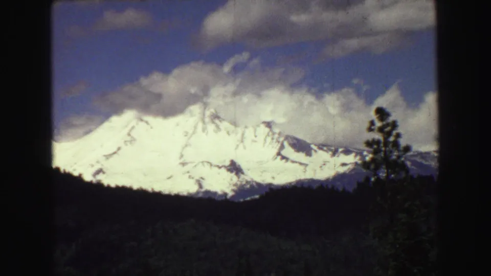 1968 8mm close landscape view near Vancouver, showing a bright snow-covered mountain above a dark forested slope and clouded sky.