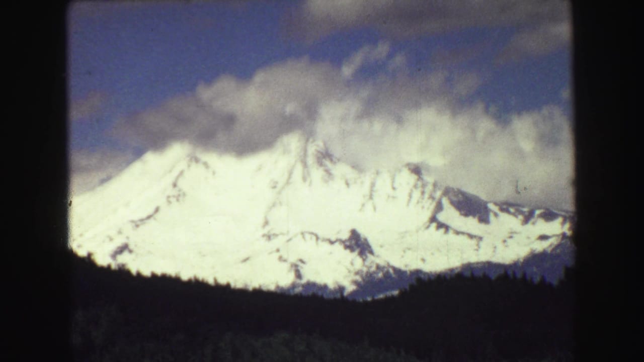 Bright snow-covered peaks under clouds with a dark forest line below.