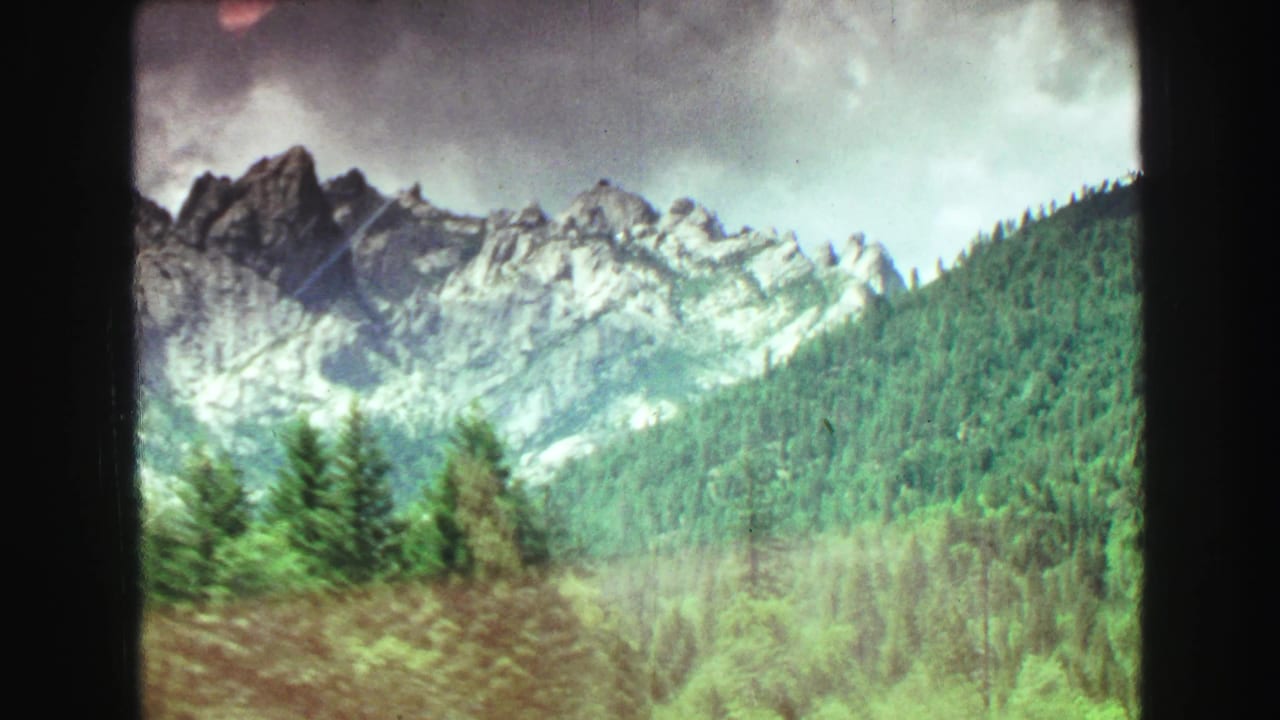 Forested mountain slopes and rocky peaks seen from a moving vehicle.
