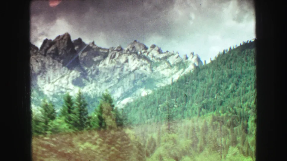 1968 8mm travel footage shows rugged forested mountains under cloudy skies, viewed from a moving car in the Vancouver, British Columbia metadata context.