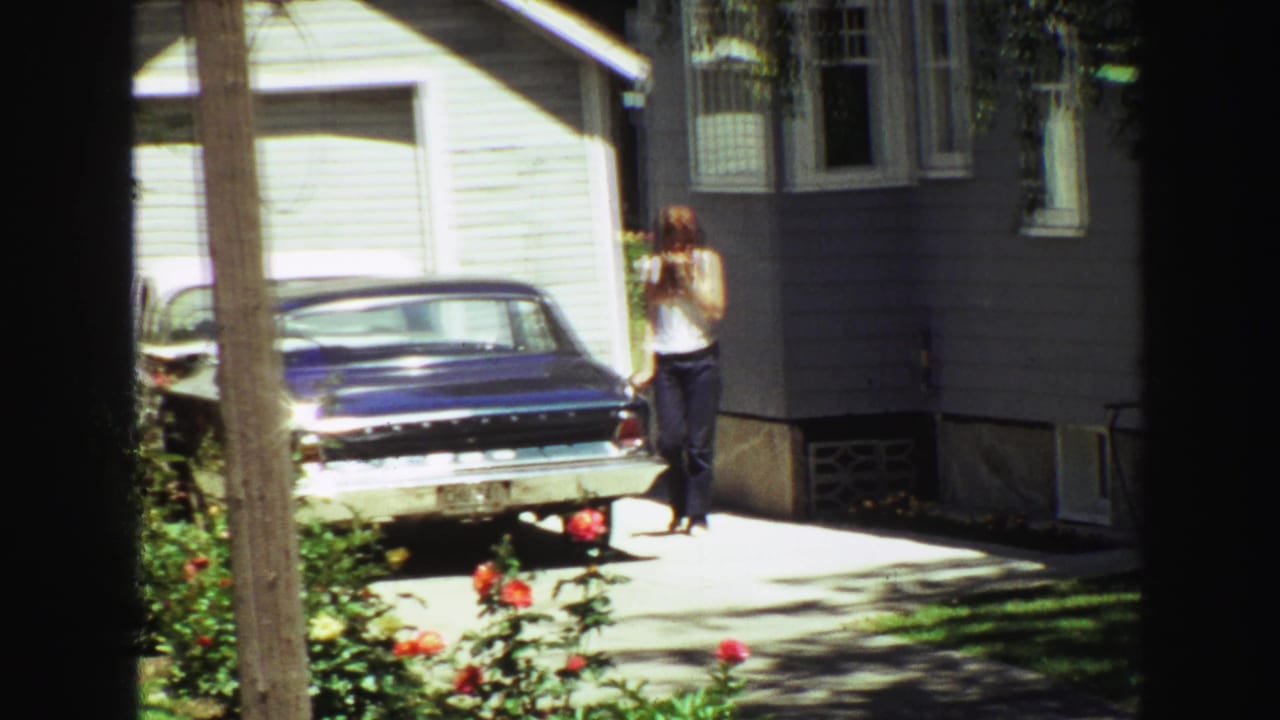 Young woman walking beside a blue sedan in a sunny driveway near a light-colored house.