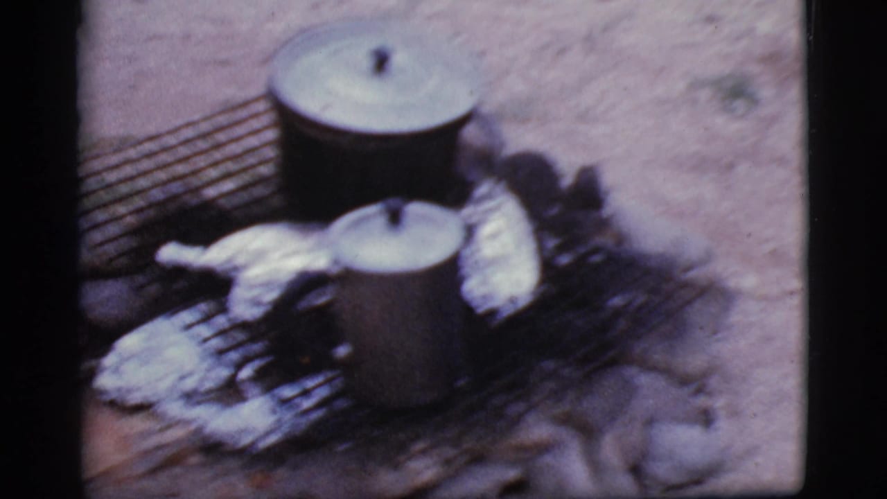 Lidded pots and foil-wrapped food sit on a grill over a small outdoor fire pit.