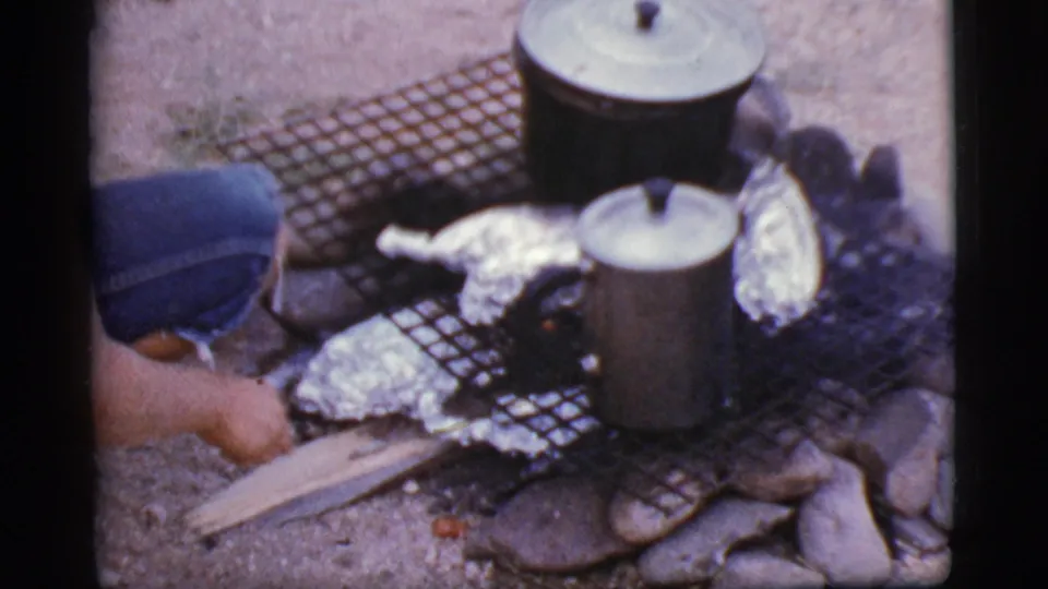 A person in blue jeans crouches beside the Cottonwood, Arizona fire pit as foil packets and cookware sit over the flames.