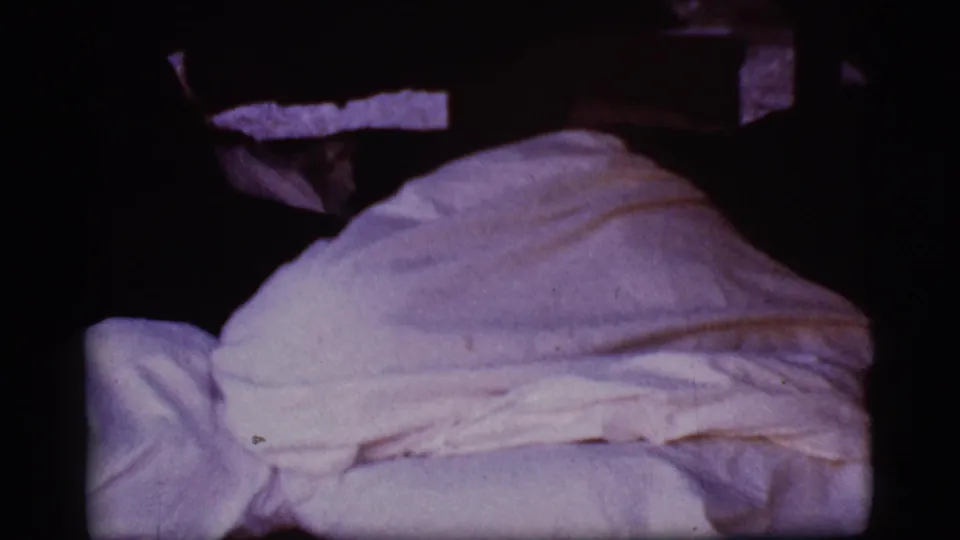 1968 Cottonwood, Arizona 8mm frame with white bedding filling the lower frame and a rounded sheet-covered form in dim light.