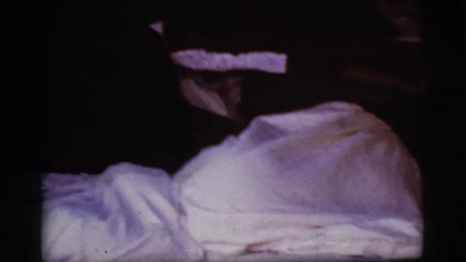 1968 Cottonwood, Arizona 8mm frame showing bunched white covers and a rounded form under dim, purple-tinted small-gauge film light.
