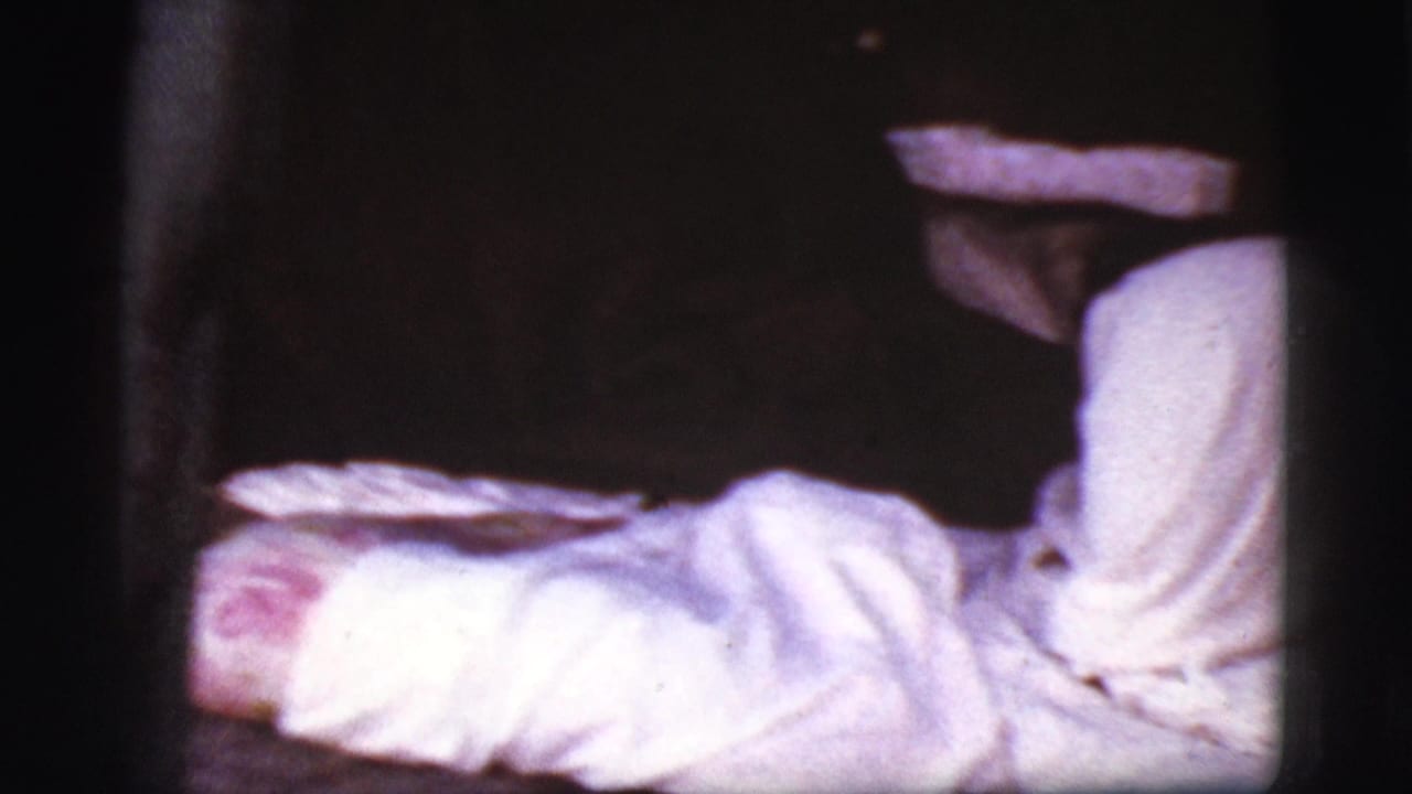 Blurred person lying under or beside a white sheet in a dark room.
