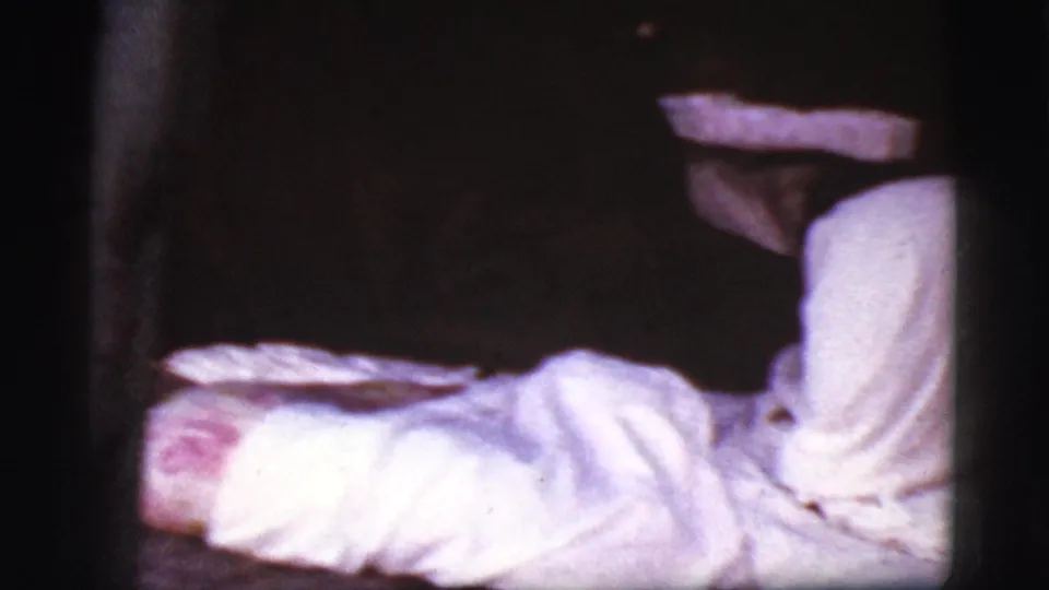 1968 Cottonwood, Arizona 8mm frame showing a blurred person reclining with a white sheet in a dim interior.